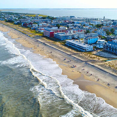 Beach scene in Rehoboth Beach, Delaware, featuring clear blue water, soft sand, and a vibrant neighbourhood houses
