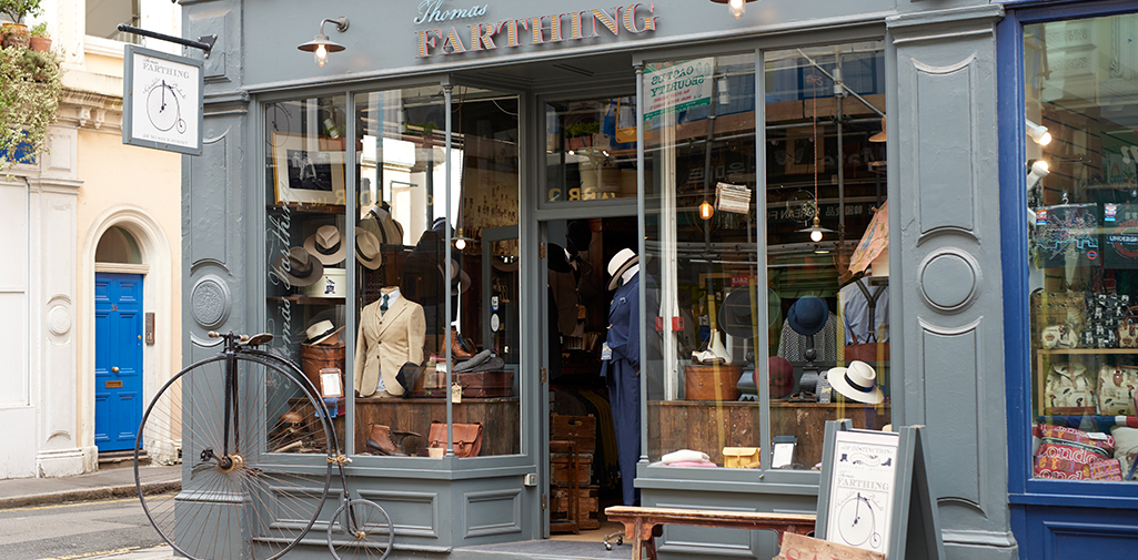 Exterior view of Thomas Farthing, a Bloomsbury menswear boutique showcasing a range of men's clothing including tweed and linen suits, knitwear, and hats.