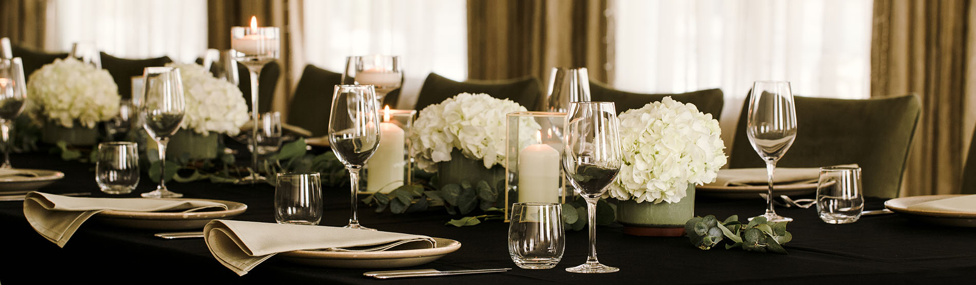 Long table set up for wedding with black table cloth, white flowers and white candles