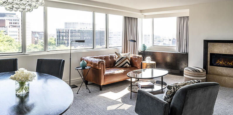 A spacious living area in the Parkview Suite at the Dupont Circle Hotel, featuring a fireplace, a sofa, a single chair, a dining table, and fresh flowers