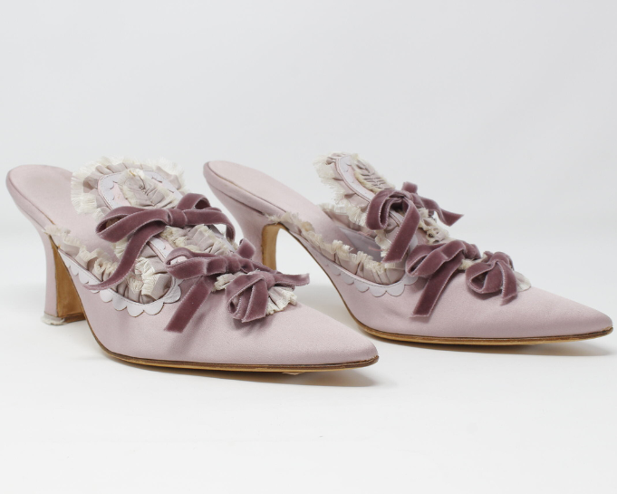A delicate, ornate pair of shoes by Marie Antoinette. Embellished with intricate embroidery and pastel tones, the shoes evoke the elegance, extravagance, and enduring influence of the 18th-century queen, set against a refined backdrop that hints at centuries of fashion and opulence.